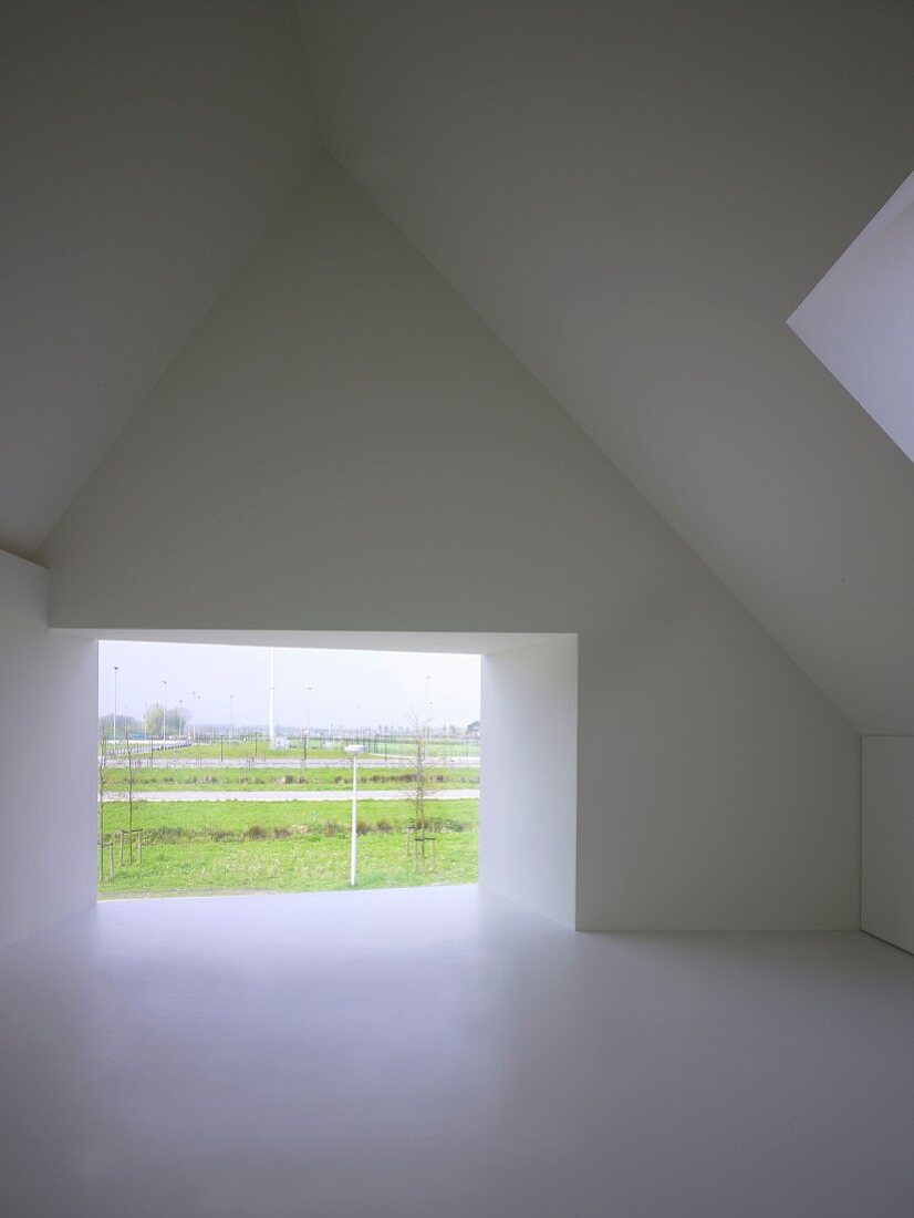 Moderner, leerer Dachraum mit rahmenlos verglaster Wandöffnung und Blick in Landschaft