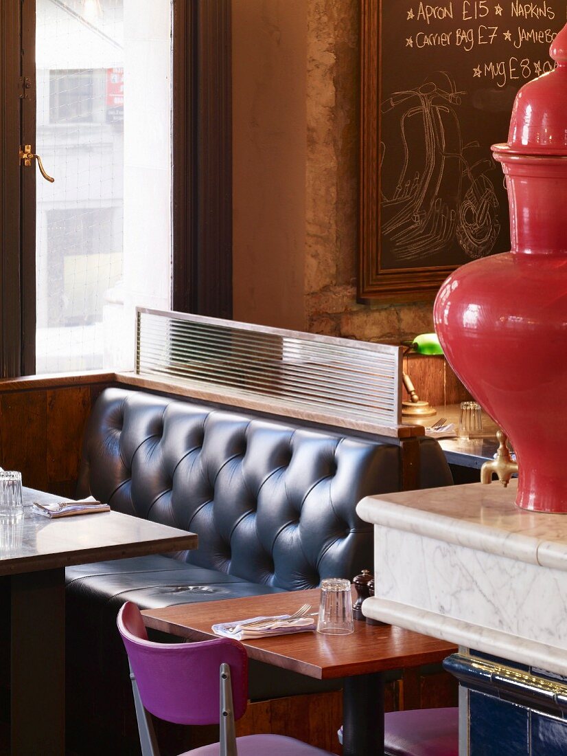 Farb- und Stilmix in englischer Coffee Bar - Lounge-Nischen im Retrostil und lila-poppige Stühle an Zweiertischchen neben Porzellan-Urne auf Marmorblock