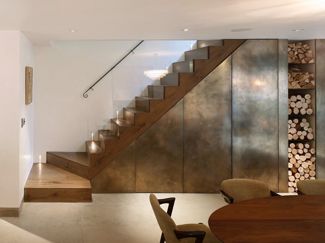 Wood block, designer staircase with glass balustrade and metal elements next to open firewood stack
