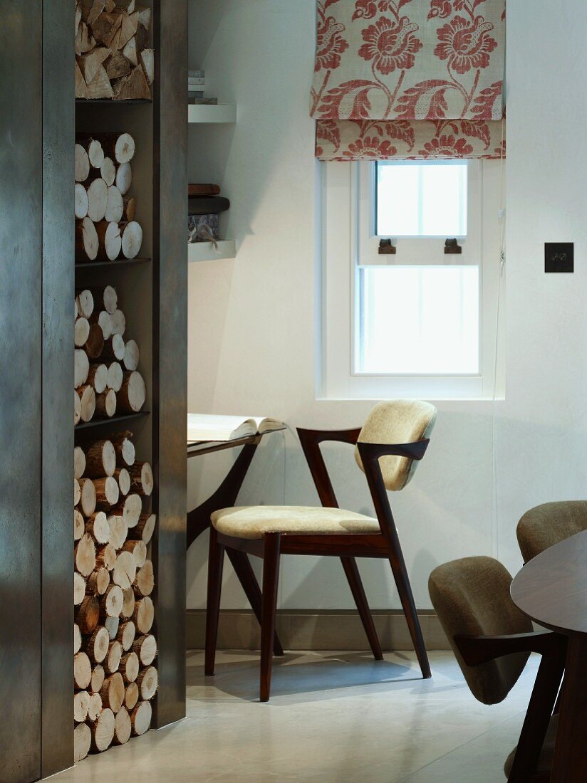Integrated firewood stack next to office niche with designer chair and Roman blind with floral pattern