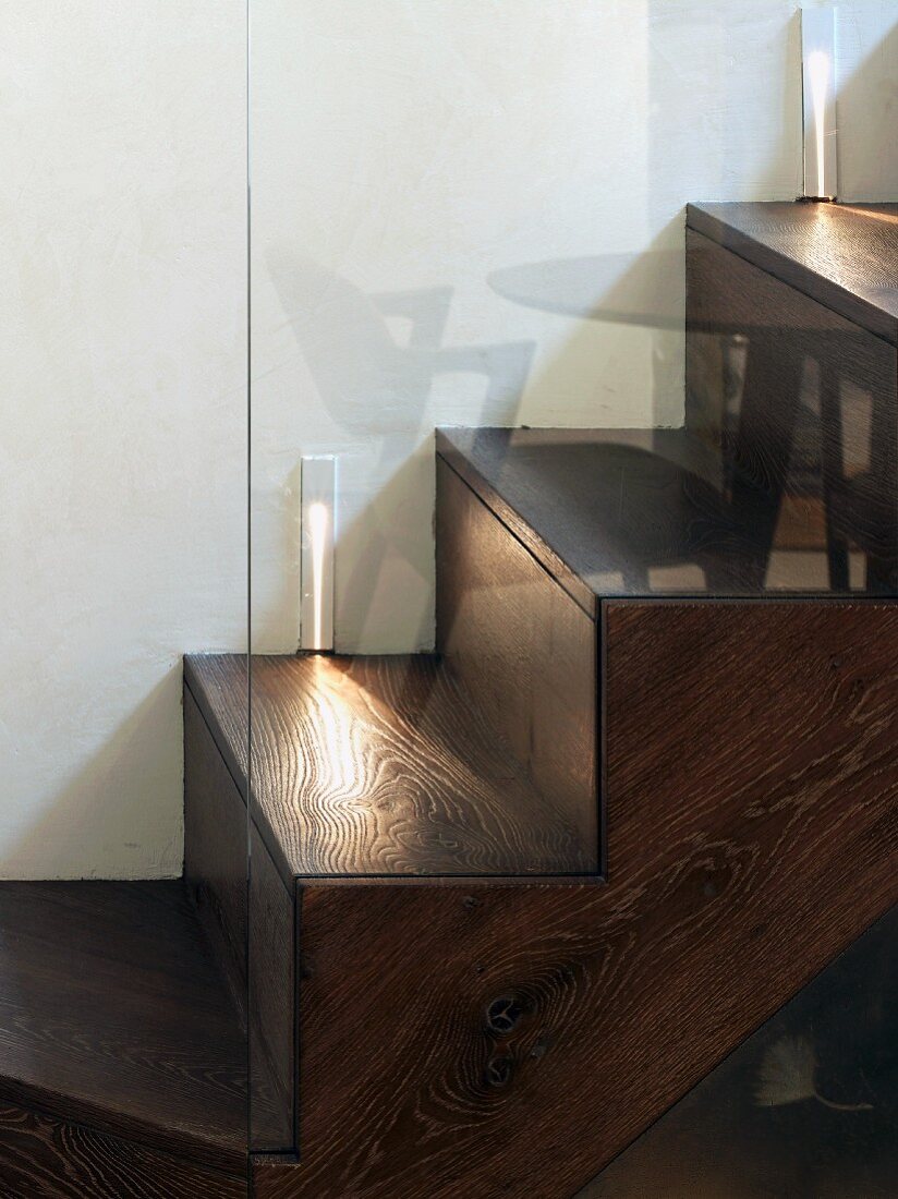 Wood-clad, concrete stairs with lighting and reflections in glass balustrade
