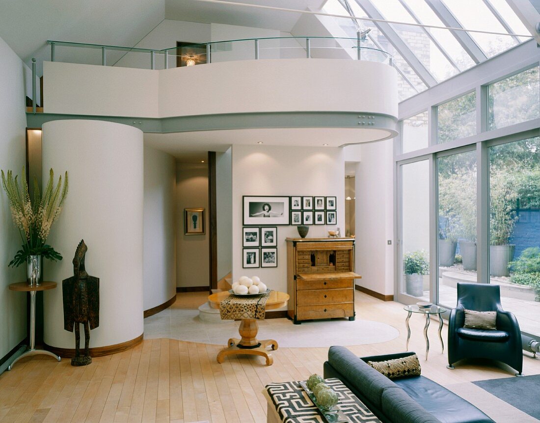 Möbel und Deko Sammlerstücke im hohen, offenen Wohnraum mit Wintergartenverglasung und gerundeter Galerie