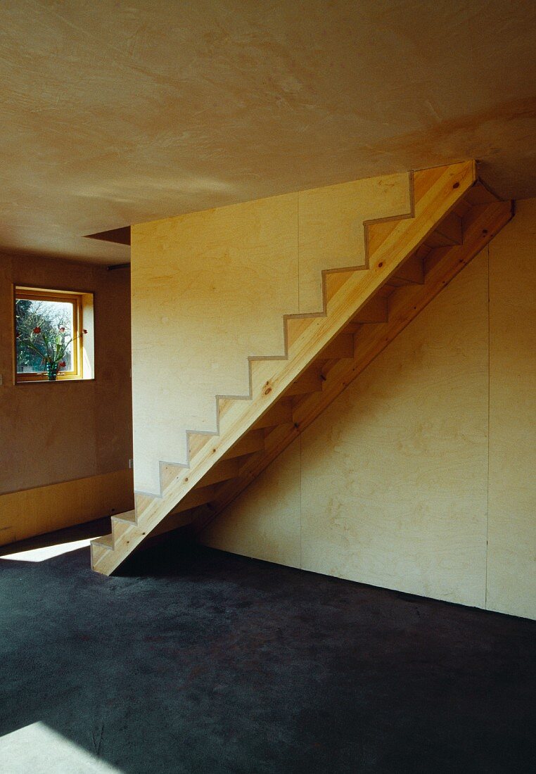Einfache Holztreppe ohne Geländer und Sonneneinfall auf Betonboden in Holzhaus mit Sperrholzverkleidung