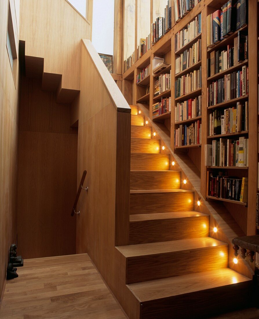 Bücherregal über beleuchteten Stufen im Treppenaufgang eines Holzhauses