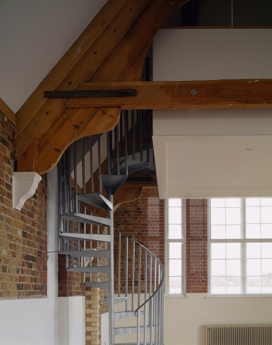 Steel spiral staircase in room with exposed brick walls & roof beams
