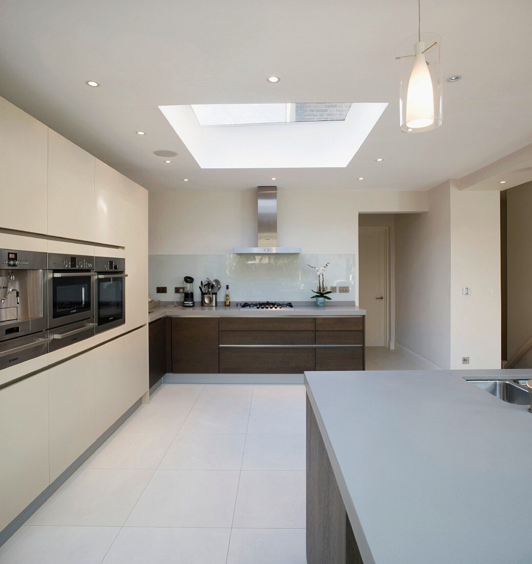 Spacious kitchen with dark wooden fronts on base units and tall cream-coloured cupboards with integrated appliances