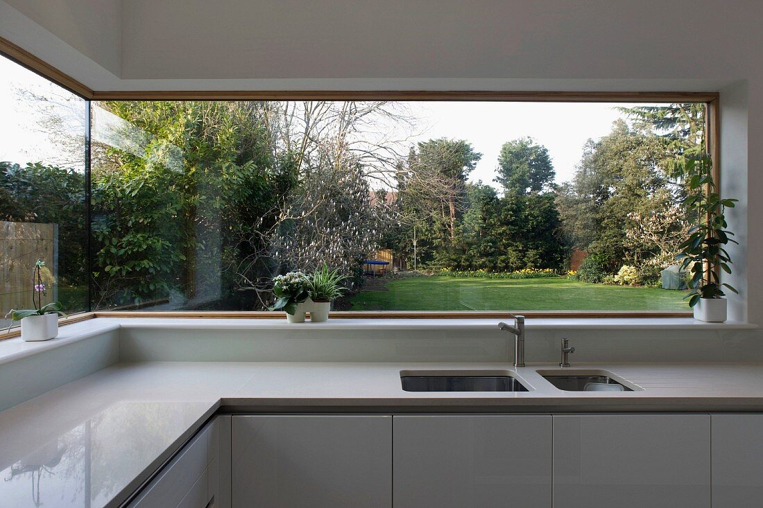 Panoramic window with view of garden in light designer kitchen with Corian work surfaces