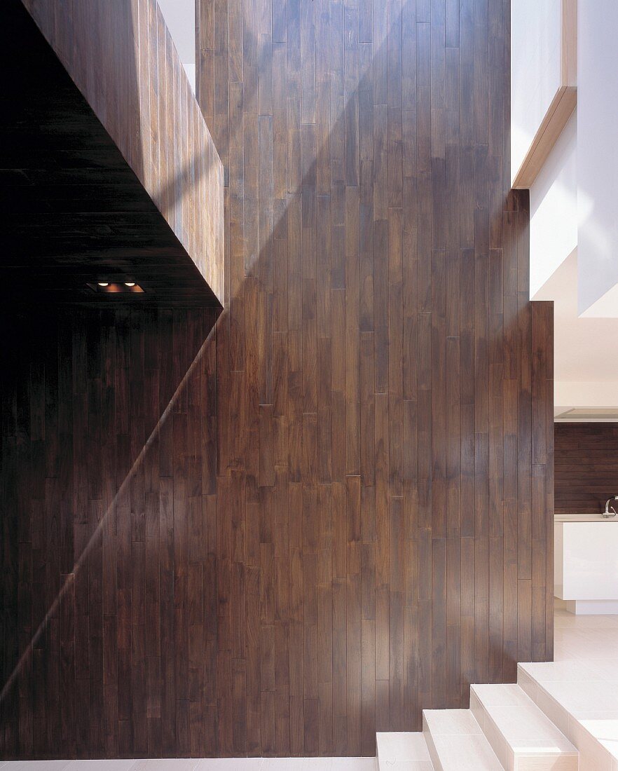 Holzverkleidete Wand in Doppelhöhe neben der Treppe