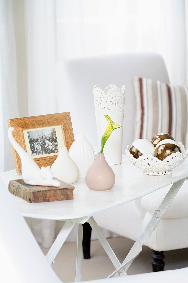 Weisser Beistelltisch mit Blumenvasen, Dekoschale, Katzenfigur und Foto