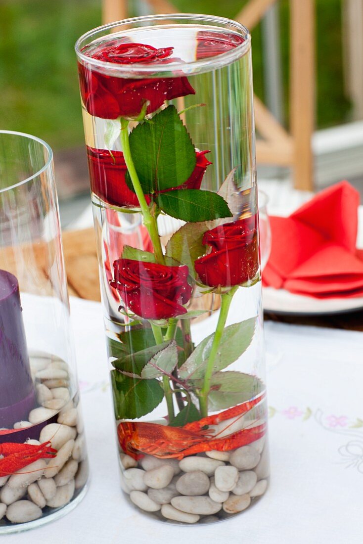 Rote Rosen mit Kieselsteinen und Flusskrebs in einer Glasvase