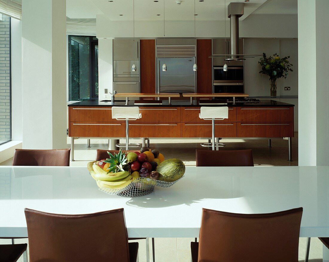 Wire fruit bowl on white dining table in front of open-plan designer kitchen