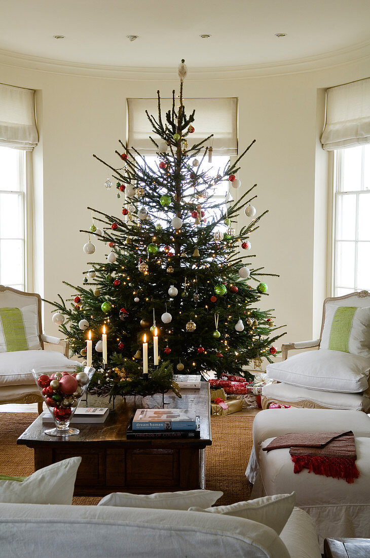 Geschmückter Weihnachtsbaum in traditionellem Wohnraum mit weissen Polsterstühlen