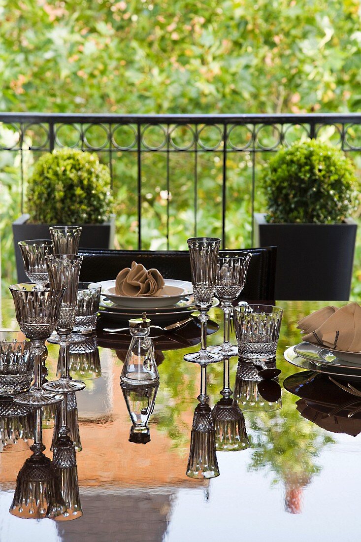 Various crystal glasses on reflective table in front of balcony with planters
