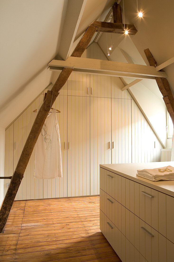 Schlichtes Dachzimmer mit Einbauschrank aus weiss lackiertem Holz an Giebelwand