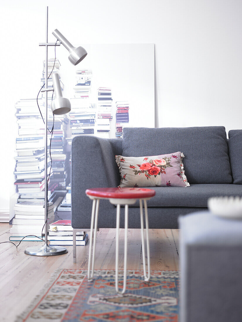 Graues Sofa mit floralem Kissen und roter Hocker in Wohnzimmer