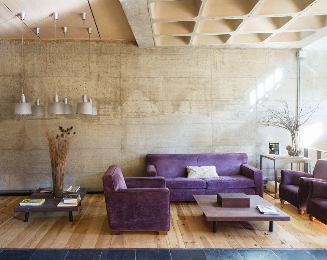 Lila Sitzgarnitur in einem Wohnzimmer mit Betonwand und Holzboden