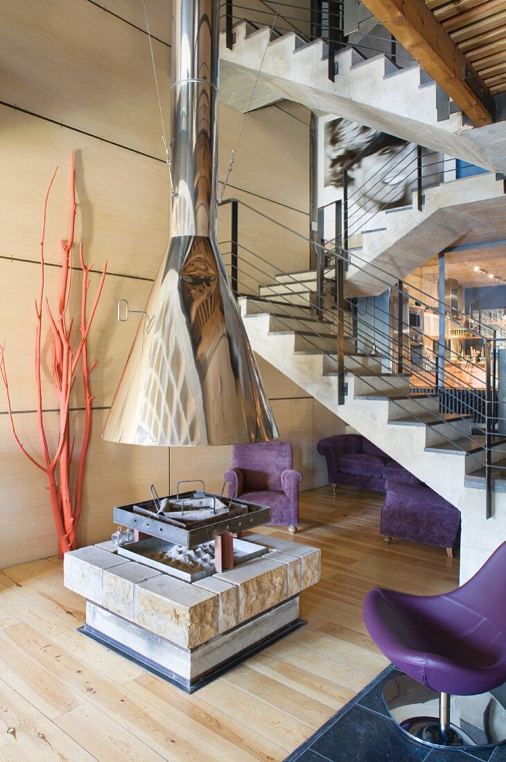 Free-standing fireplace with stainless steel flue in open-plan interior with simple concrete staircase in background