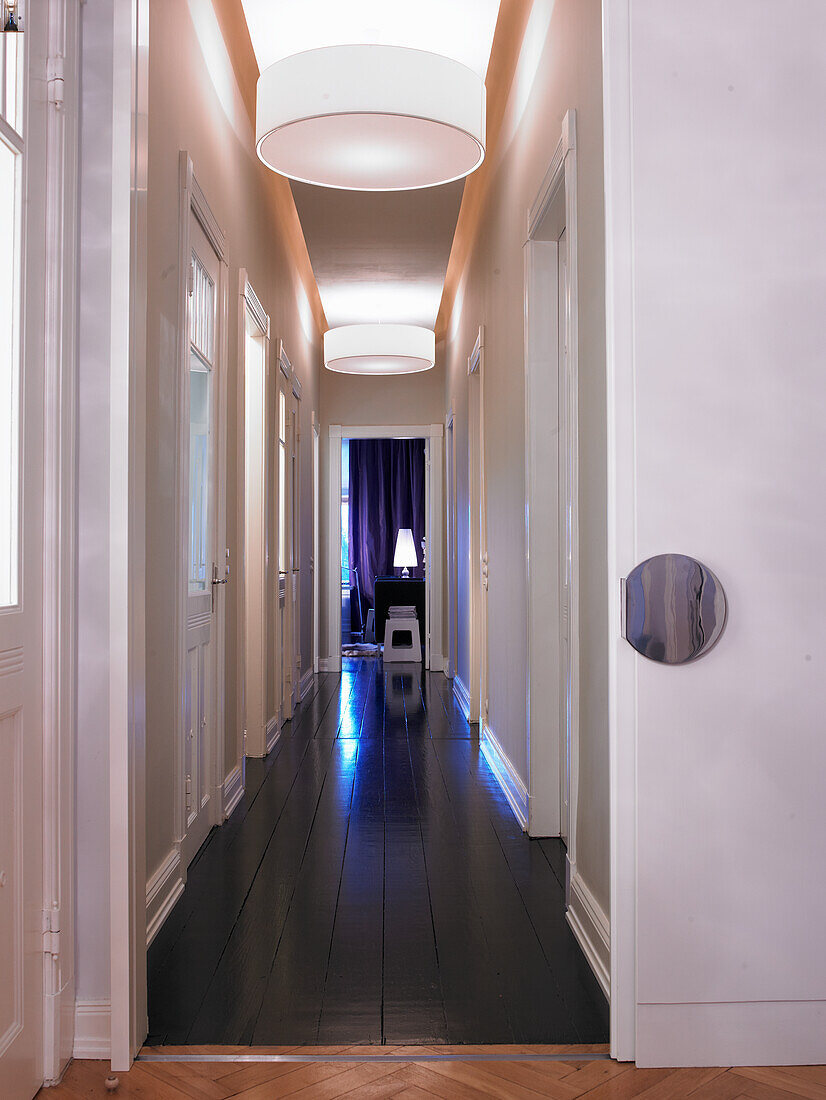 Long hallway with dark wooden floor and white ceiling lights