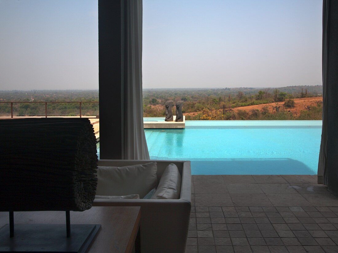 Blick von überdachter Terrasse auf Pool vor indischer Landschaft