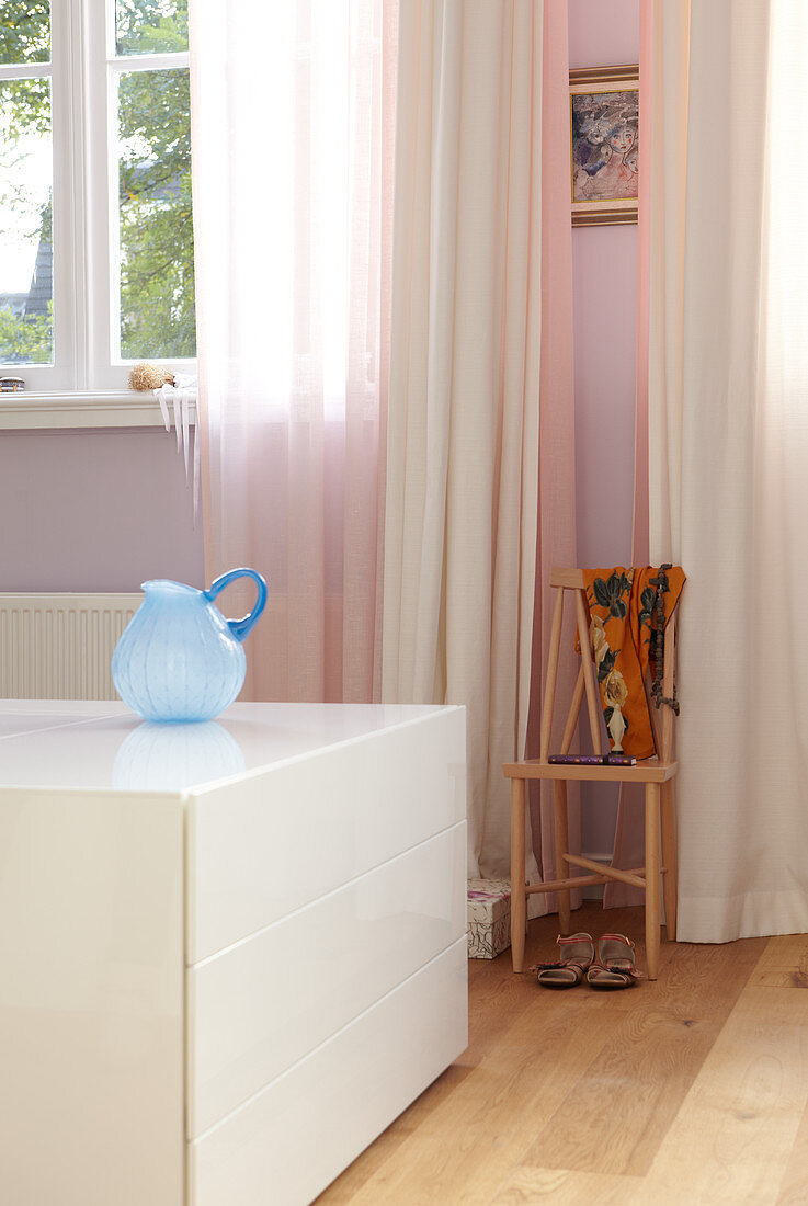 Weisser halbhoher Schubladenschrank im Raum und Fenster mit rosa-weissen Vorhängen
