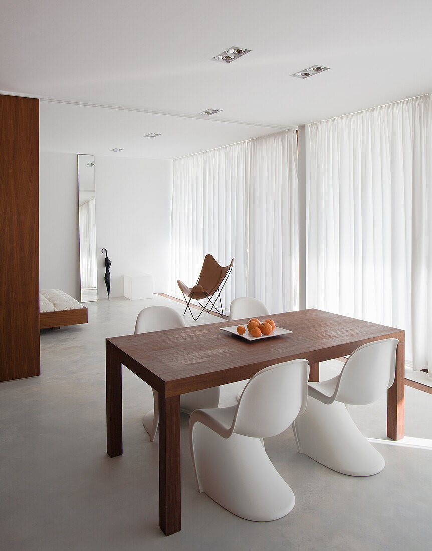 Minimalist dining room with wooden table, white chairs and full-length curtains