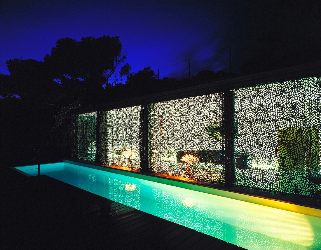 Terrasse mit Pool und Blick durch die Vorhänge in das beleuchtete Wohnzimmer