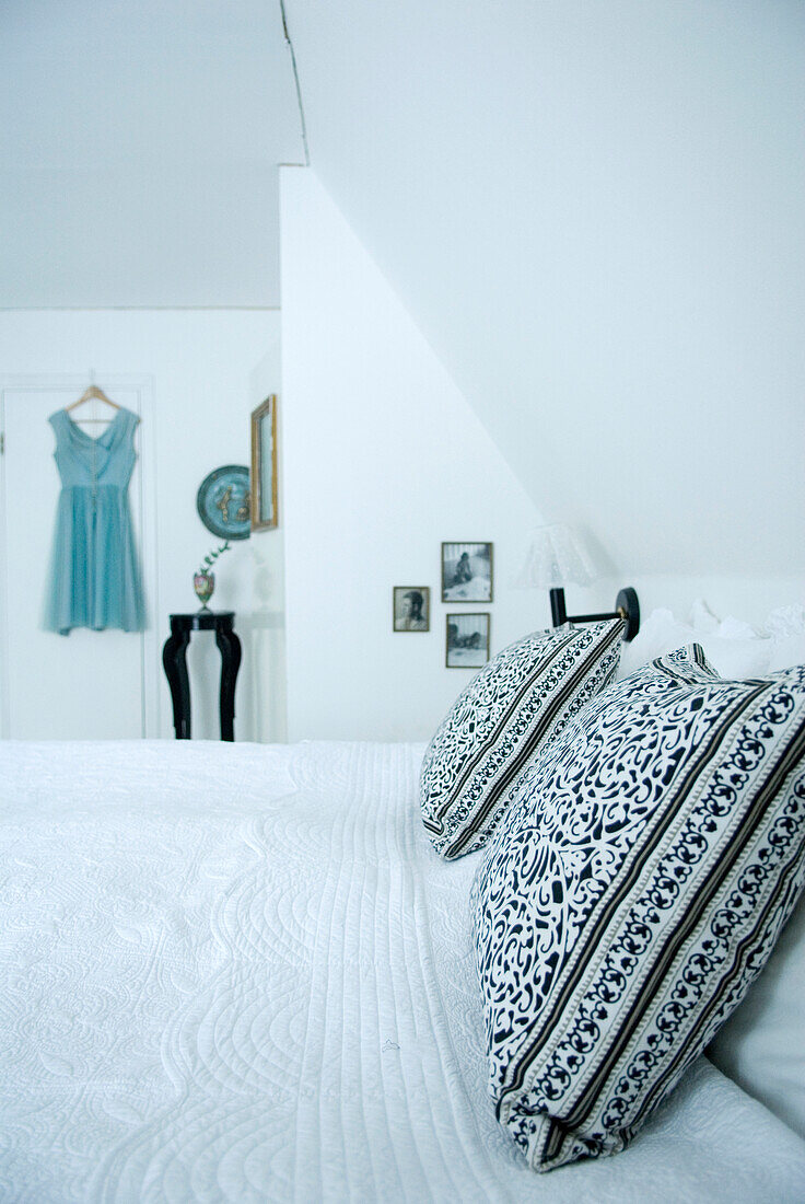White bedroom with decorative pillows and dress on the wall