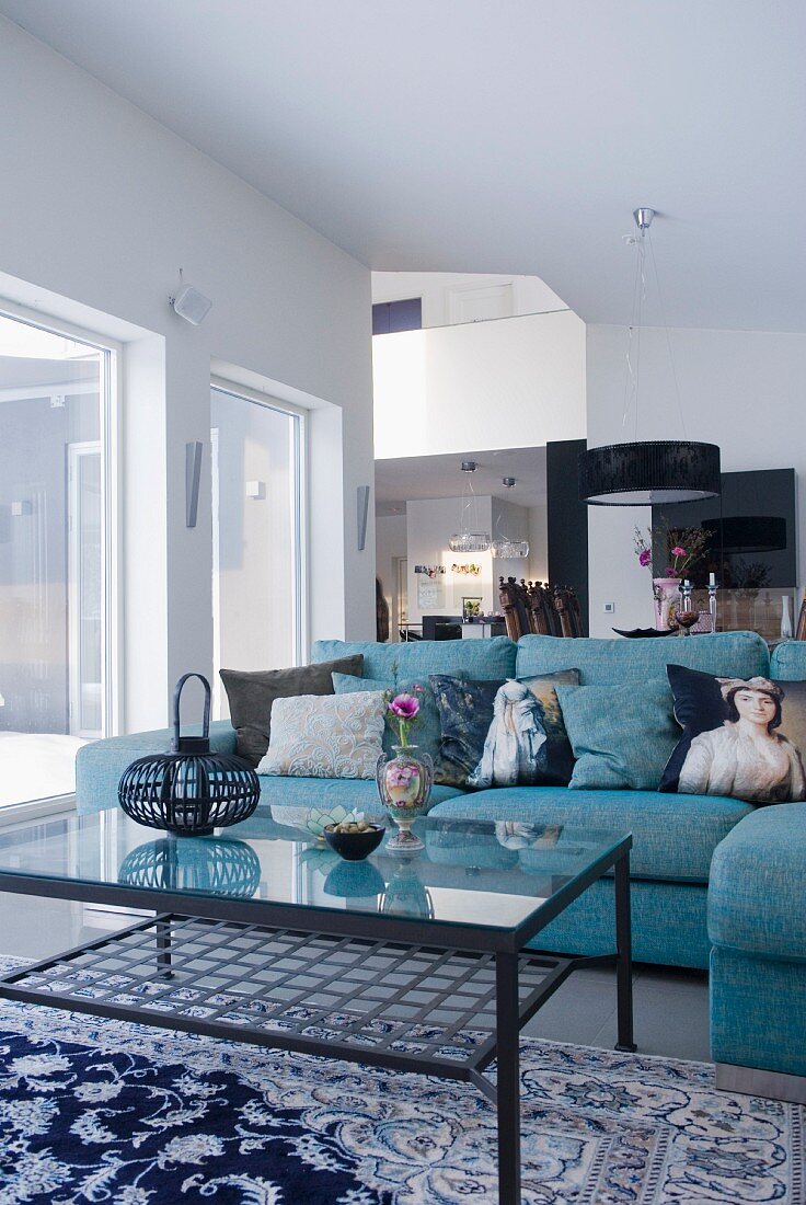 A blue corner sofa with decorative cushions and a metal and glass coffee table in a modern room