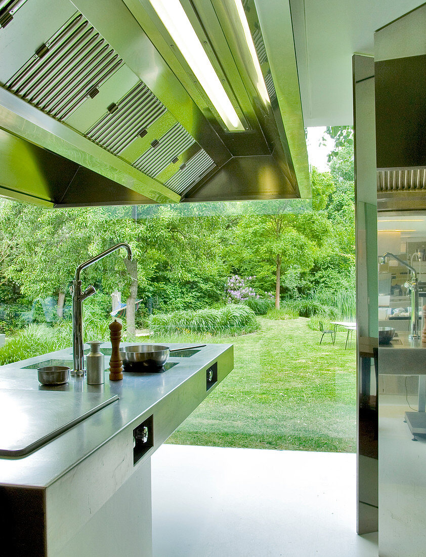 Stainless steel designer hob with extractor hood in front of glass wall of house with garden