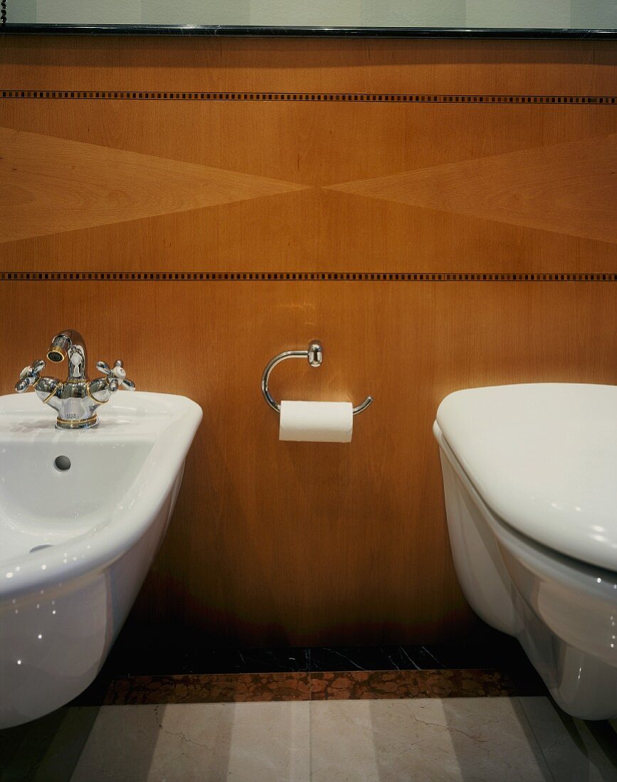 Wall-hung bidet and toilet on wood-panelled wall