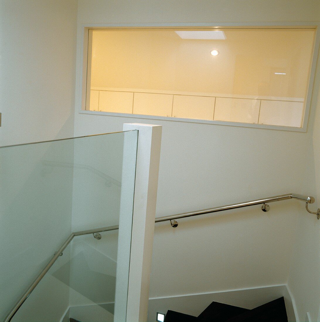 Stainless steel handrail on wall and illuminated window in white stairwell