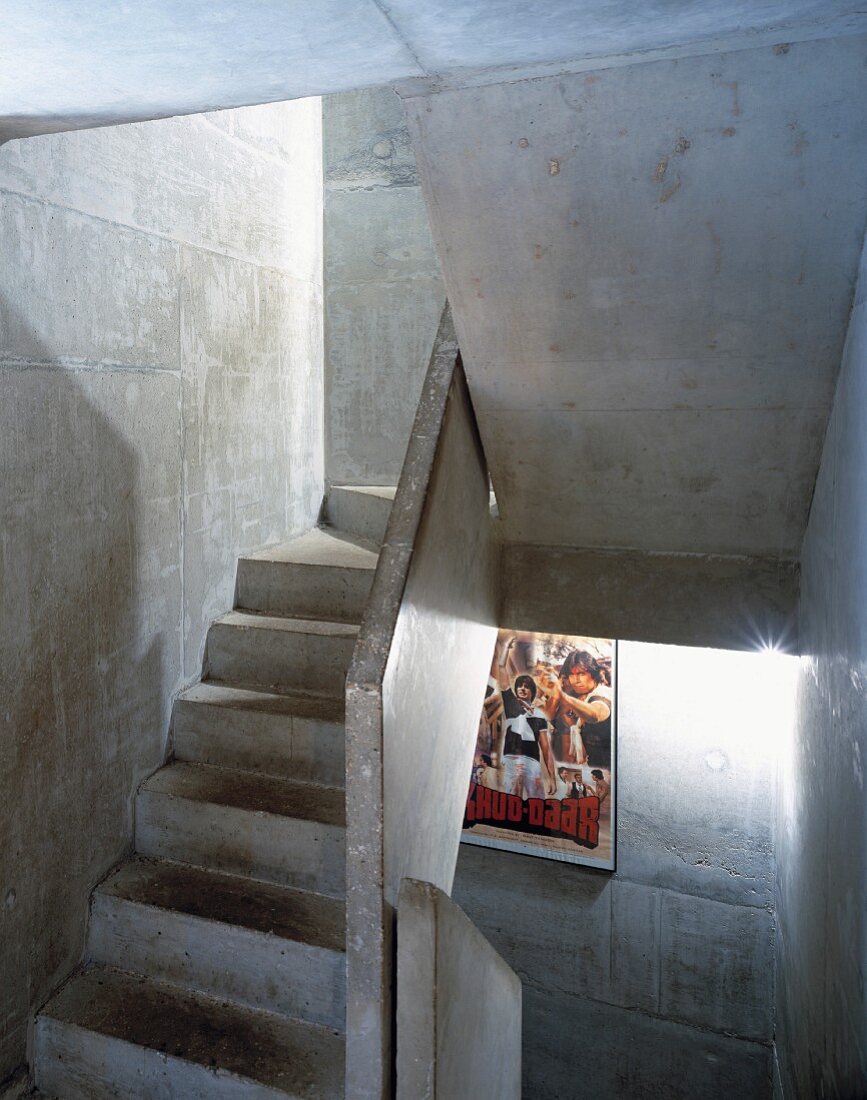 Treppenhaus aus Beton mit beleuchtetem Kinoplakat an Wand