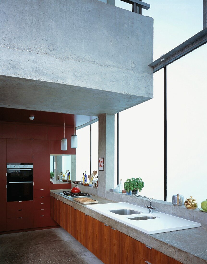 Küchenzeile an Fensterfront und darüber schwebende Galerie aus Beton