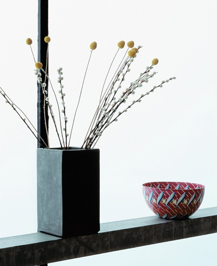 Shelf with twigs in concrete vase next to bowl with fish motif
