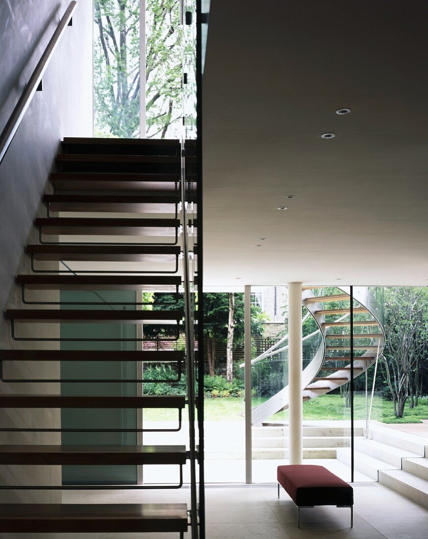 Treppe mit Holzstufen im offenen Wohnraum und Blick durch Terrassenfenster auf Aussentreppe