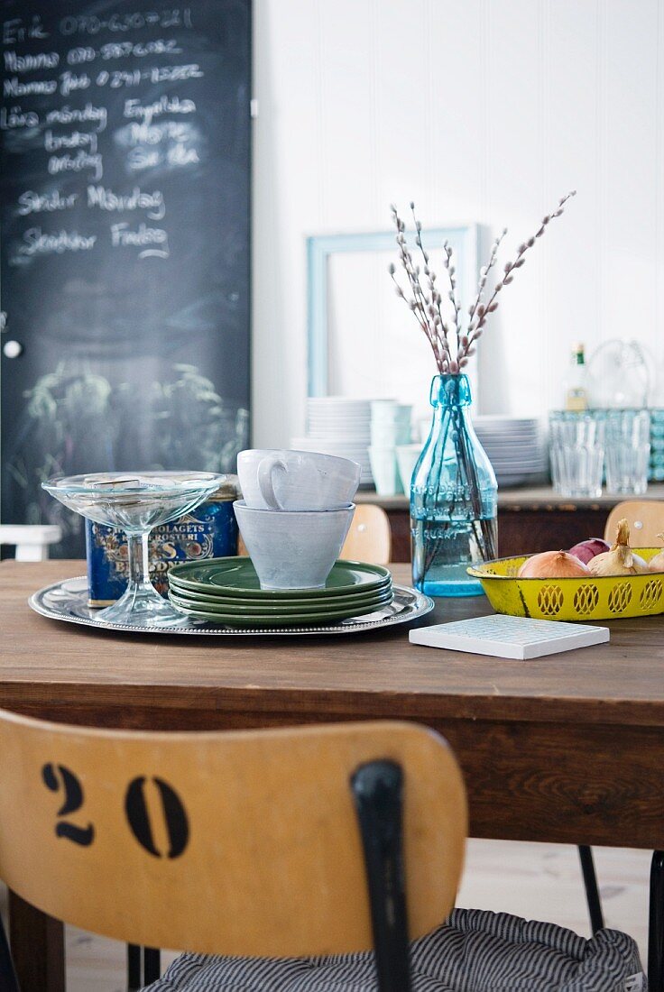 Holztisch mit Tellern und Tassen, im Hintergrund Ablage mit Geschirr und grosse Kreidetafel in einem Esszimmer