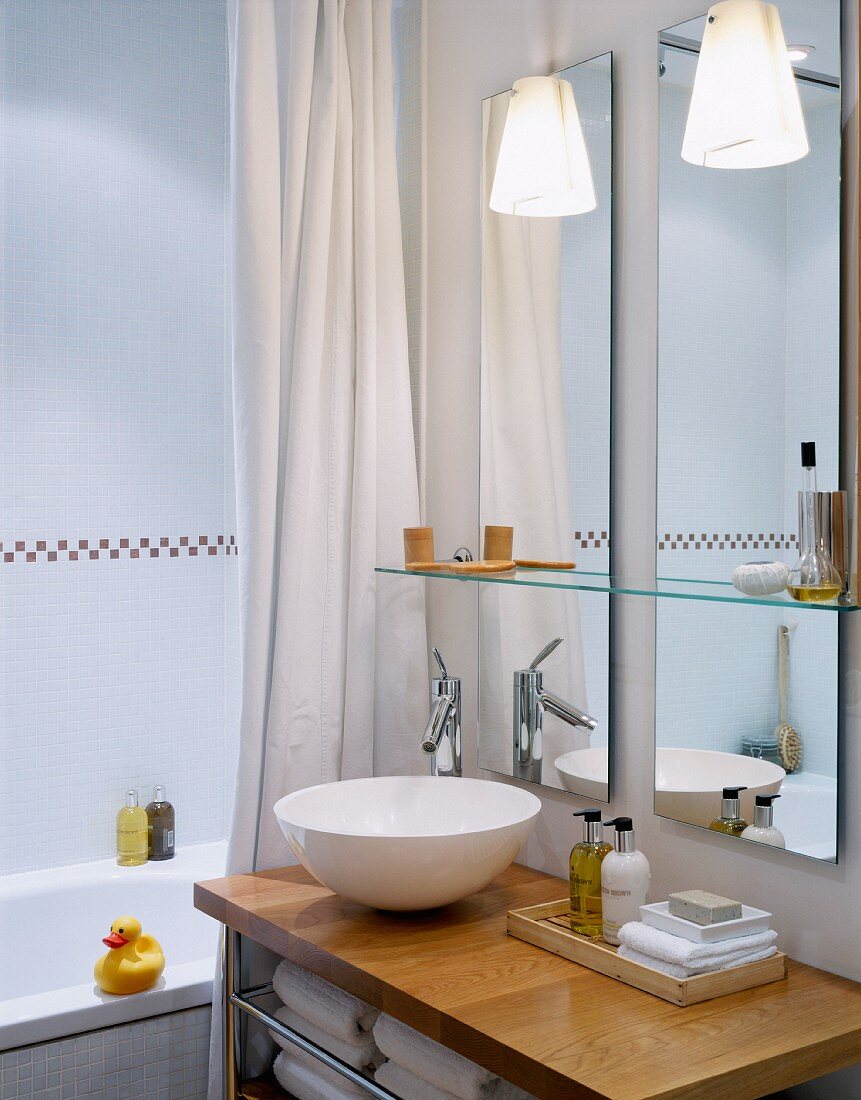 weiße Waschschüssel auf Holzplatte vor Wandspiegel im modernen Bad