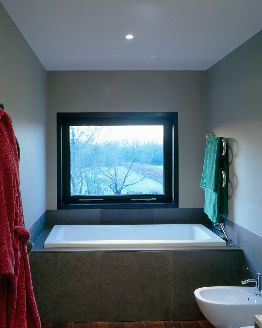 Vor Fenster eingebaute Badewanne mit grauer Fliesenverkleidung