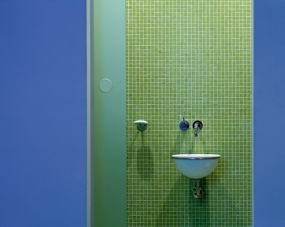 View of designer wash basin on wall with green mosaic tiles through open door