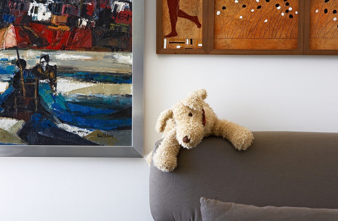 Small plush dog on back of upholstered sofa and various paintings on wall