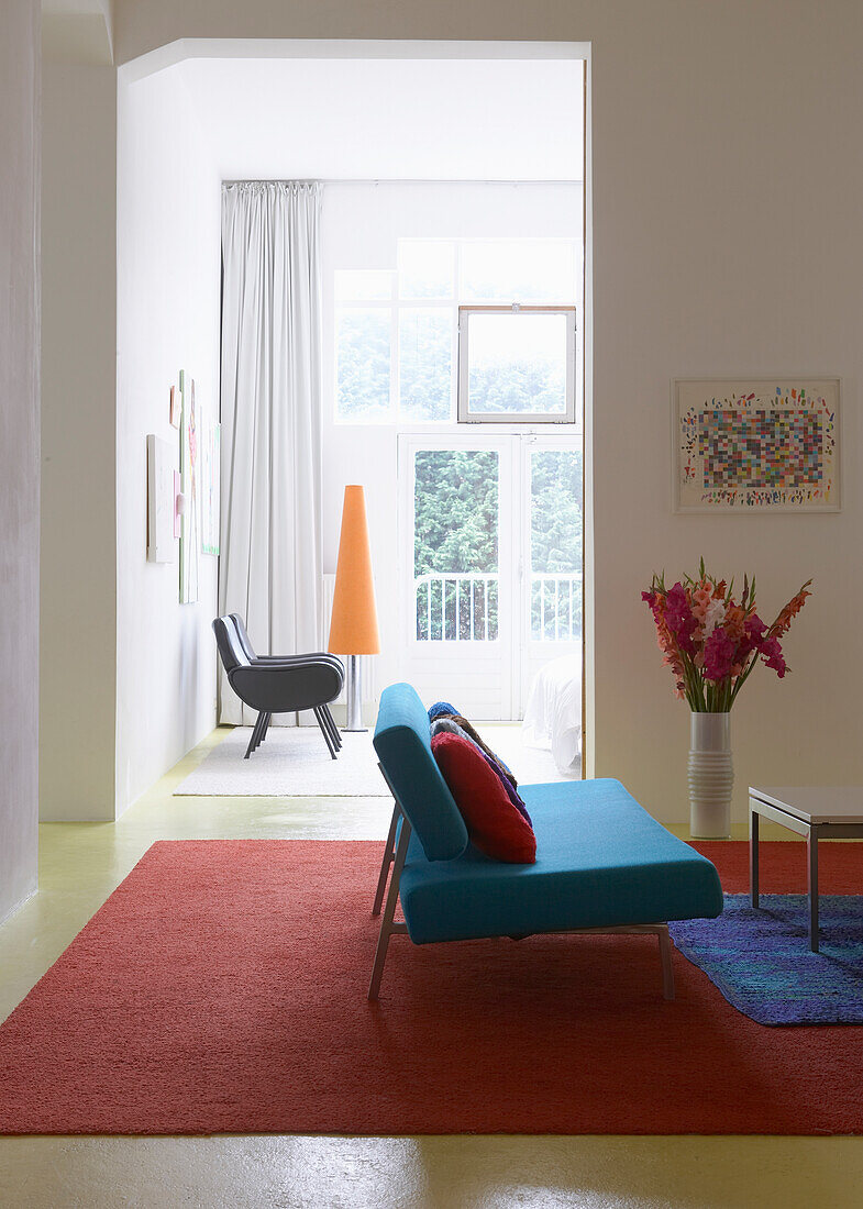 Wohnzimmer mit rotem Teppich, blauem Sofa und Bodenvase