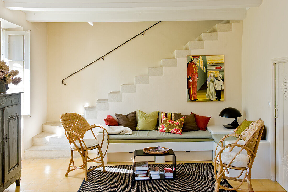 Living room with staircase, rattan armchairs and colourful cushions