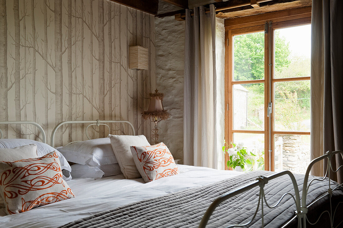 Bedroom with metal bed, wallpaper with tree motif and rustic charm