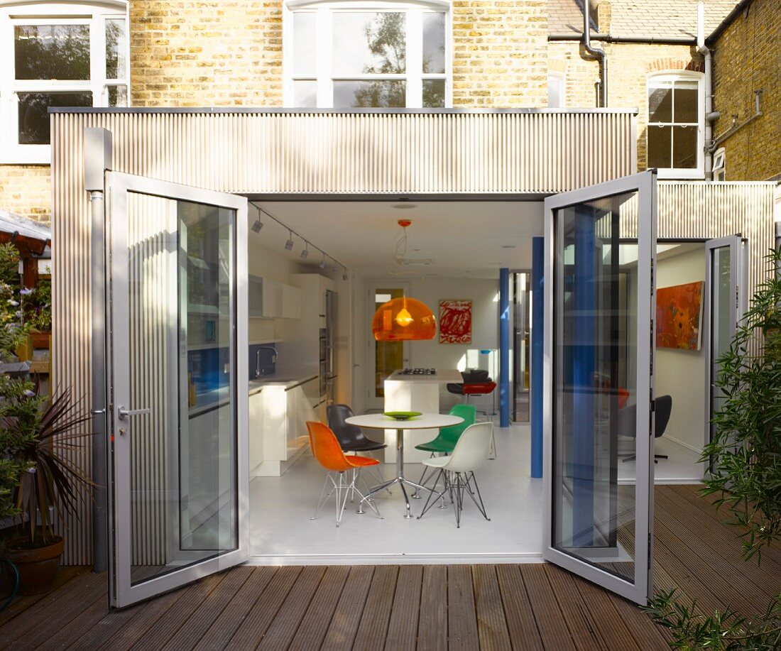 Extension with wooden terrace and open glass door with view of modern dining area