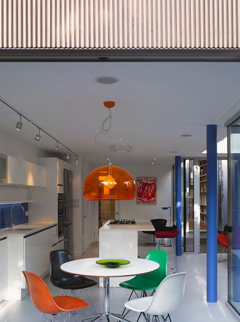 Dining area with colourful shell chairs and pendant lamp with orange glass shade