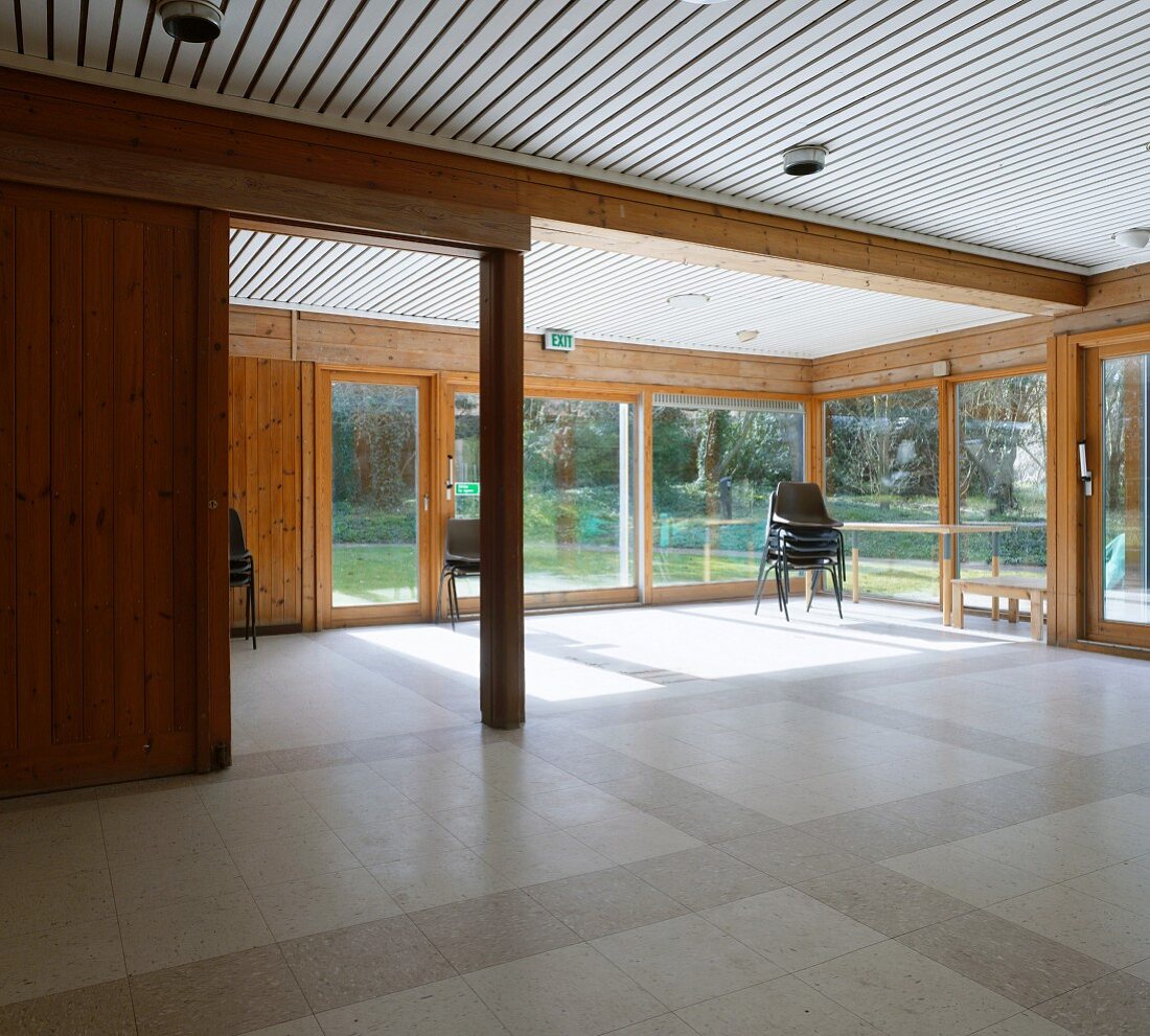 Leerer Wohnraum im modernen Holzhaus mit raumhohen Terrassenfenstern und Gartenblick
