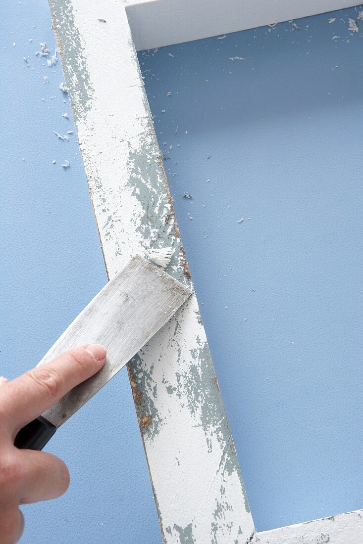 Old, white-painted wooden frame being worked on with scraper