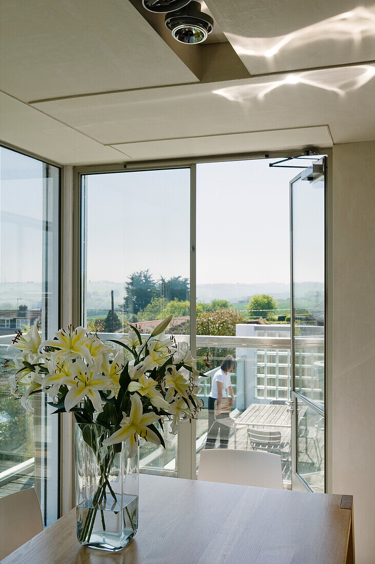 Vase mit Lilien auf einem Tisch in einem modernen Esszimmer mit Panoramafenstern