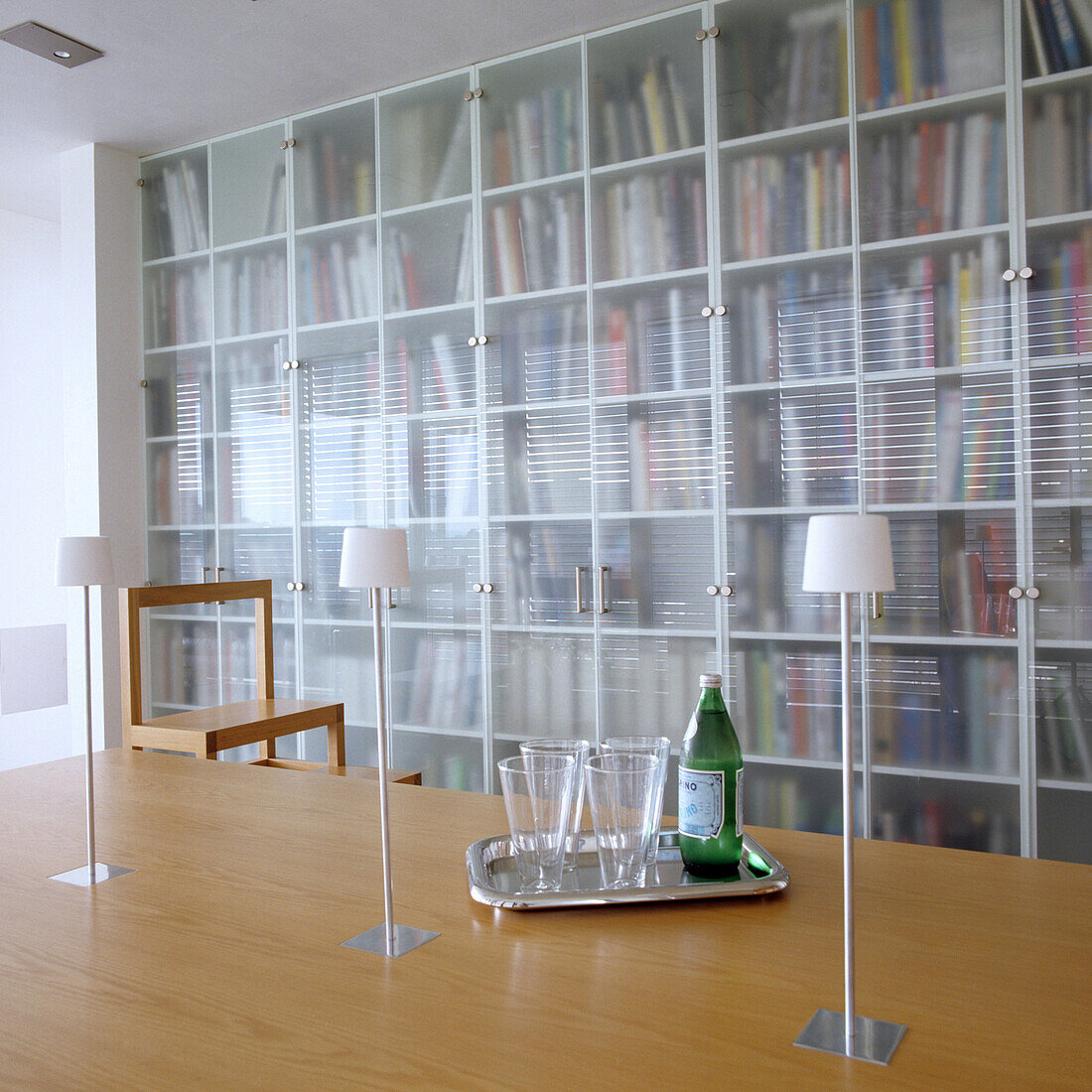 Dining table with table lamps and bookshelf with frosted glass doors in the background