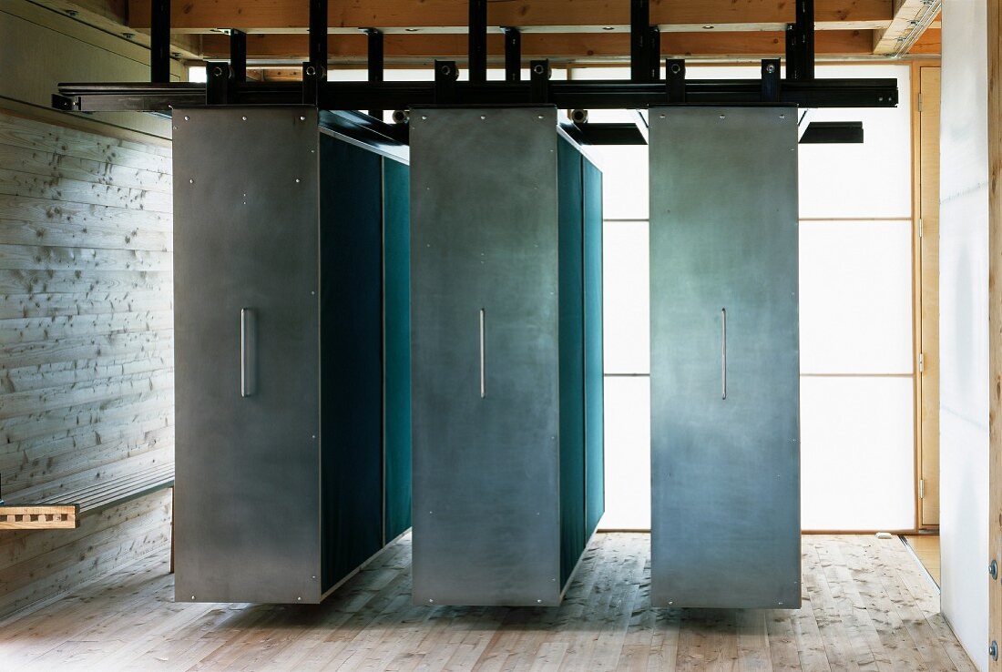 Suspended, moveable cupboards with steel doors in front of translucent walls in contemporary house